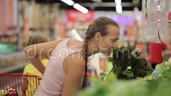 年轻的母亲带着小女儿在手推车里挑选超市里的蔬菜视频的预览图