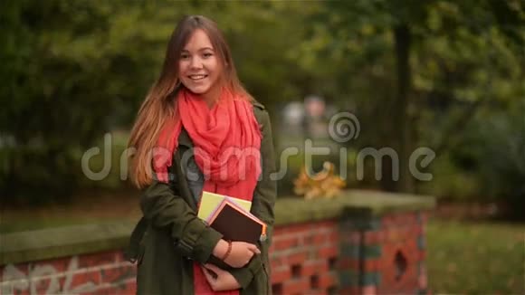 快乐的学生女孩开心地笑着快乐地在五彩缤纷的秋天公园里捧着书视频的预览图