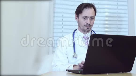 办公室里的医生在笔记本电脑上工作穿着白色外套和领带的人在笔记本电脑上的办公室里工作视频的预览图