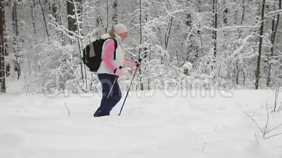 穿着温暖运动服的女人背着背包积极地走在森林里的小径上手里拿着一只手视频的预览图