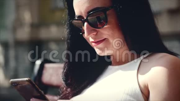 一个漂亮的商界女性一个高加索人的外表使用智能手机技术应用程序坐在长凳上的城市街道上视频的预览图