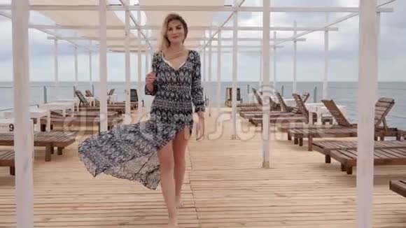 美丽的女人光着脚沿着码头走海边的女性微风的服装海边的女孩放松视频的预览图