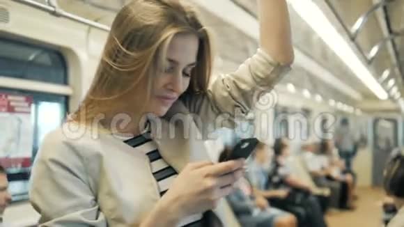 地铁列车上一位微笑可爱的女孩在手机上打字留言的肖像一位金发女学生与视频的预览图