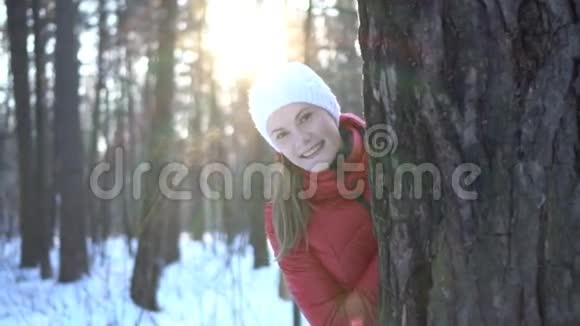 冬天公园里美丽的年轻女子躲在树后面微笑着玩得很开心慢动作录像视频的预览图