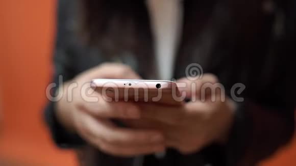 年轻的女人手拿手机在橙色的背景上视频的预览图
