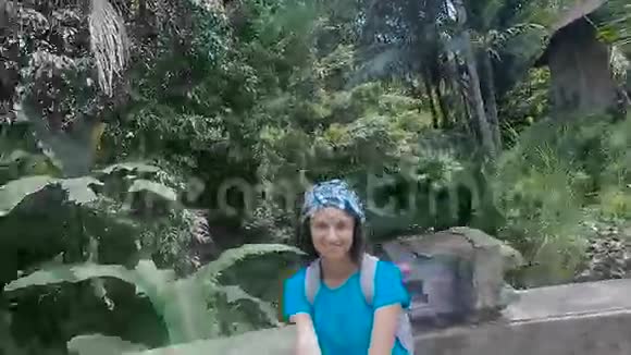 巴厘岛在岛上游览穿蓝色衬衫的女孩走在石桥上深色头发的女人视频的预览图