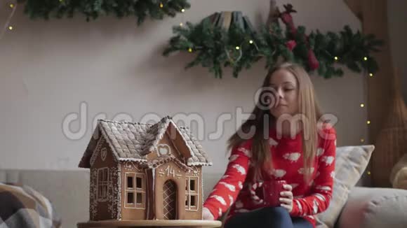 一位穿着冬装的美女在家附近的圣诞树旁喝着带姜饼的茶视频的预览图