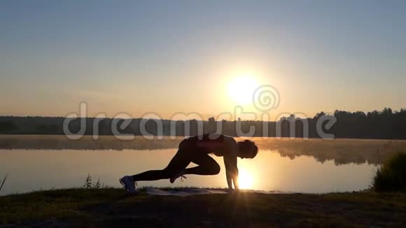 日落时分一个苗条的女人在湖岸训练健身视频的预览图