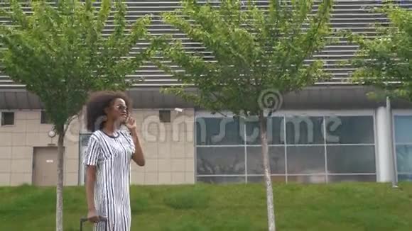 站在一旁看着迷人的年轻微笑的非洲裔美国商界女性戴着太阳镜一边等待一边用手机说话视频的预览图