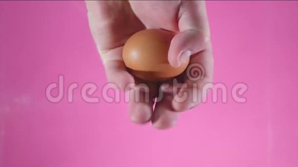 一只手握在拳头上在粉红色的背景上打碎了一个鸡蛋视频的预览图