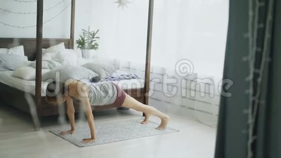 在家的卧室里在床边做瑜伽运动的快乐迷人的女人视频的预览图
