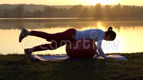 性感的女人躺在健身球上在日落时抬起一条腿视频的预览图
