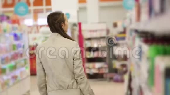 在超市的美容区带着购物篮走路的年轻女子视频的预览图