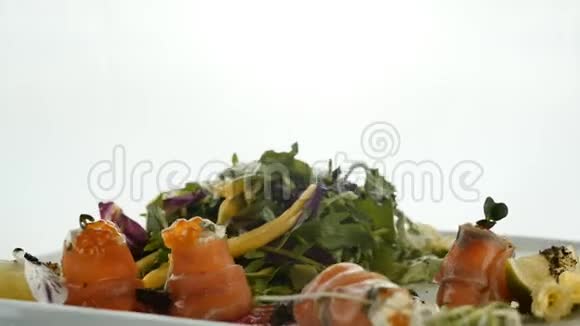 美味的红鱼或三文鱼卷与果冻橙鱼子酱和绿色沙拉混合在盘子上模糊的彩色背景视频的预览图