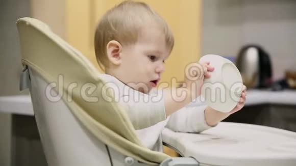 小男孩坐在厨房和盘子里的儿童座位上是非常美味的食物微笑和玩耍视频的预览图