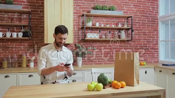 男人在家厨房用手机浏览英俊的年轻人在智能手机上浏览微笑着快乐一个男人吃视频的预览图