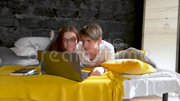 情侣躺在床上使用笔记本电脑快乐微笑在线聊天女孩和男人在卧室的早晨视频的预览图
