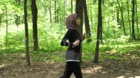 年轻运动女孩戴着头巾跑步在绿色公园慢跑侧视50英尺视频的预览图