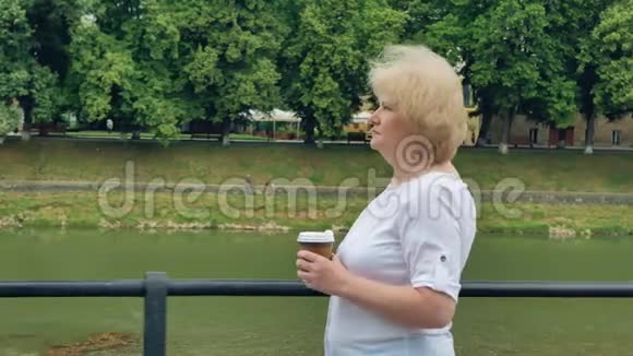 快乐的老妇人沿着海滨散步喝咖啡河流的背景视频的预览图