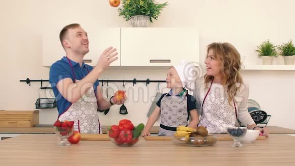 一家人正在厨房准备沙拉爸爸把苹果扔了起来儿子和他母亲在微笑视频的预览图