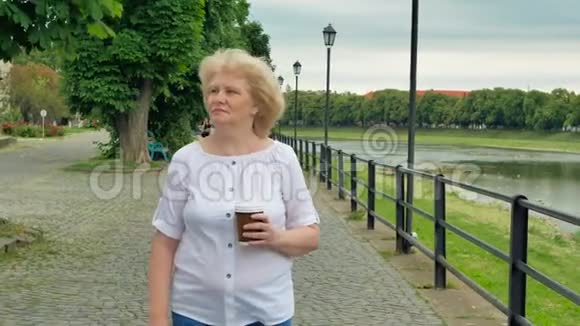 快乐的老妇人沿着海滨散步喝咖啡河流的背景视频的预览图