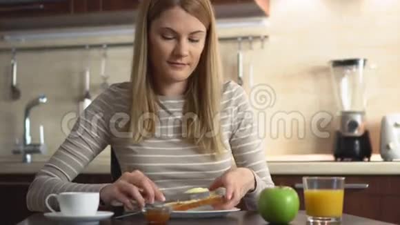 漂亮的年轻人吃面包和黄油和果酱厨房里有咖啡和果汁的早餐视频的预览图