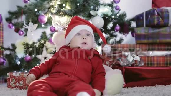 穿着红色圣诞老人服装的小男孩躺在圣诞树下视频的预览图