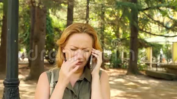 女人感到悲伤和哭泣在手机上和别人说话在夏天的公园里4k慢动作视频的预览图