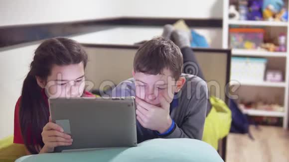 男孩和女孩躺在床上玩平板电脑男孩和女孩青少年社交媒体互联网上的平板电脑户外视频的预览图