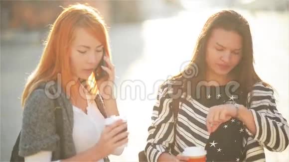 两个可爱的女孩在城里的街道上女孩们拿着纸杯喝咖啡一个红头发的女孩视频的预览图