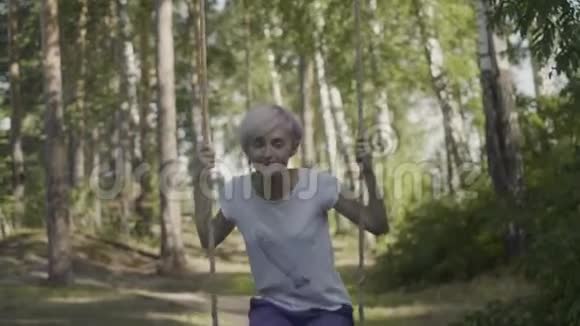 美丽的女孩在森林里的秋千上年轻女子在森林里荡秋千视频的预览图