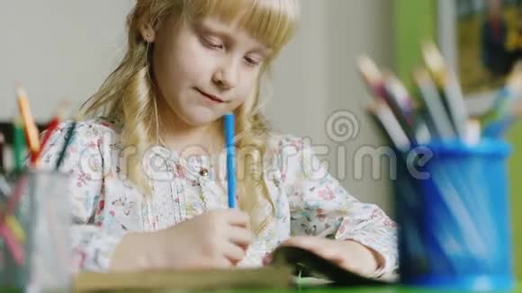 严肃的金发女孩在桌子旁画画在前景中一个有彩色铅笔的花瓶视频的预览图