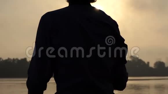 年轻的金发男子站在夕阳下一片美丽的河岸上视频的预览图