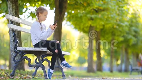 可爱的小女孩在美丽的秋日户外秋天的长椅上可爱的孩子视频的预览图
