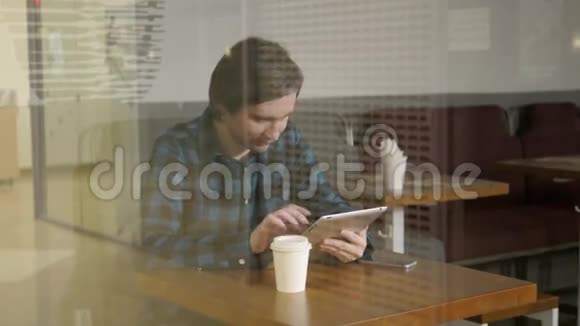 在咖啡馆工作的年轻企业家在带眼镜手机和笔记本电脑的餐馆里看橱窗的自由职业者视频的预览图