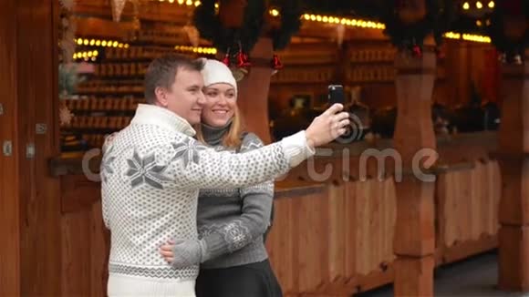 一对年轻漂亮的情侣在圣诞市场上用智能手机自拍年轻的家庭在圣诞节大笑视频的预览图