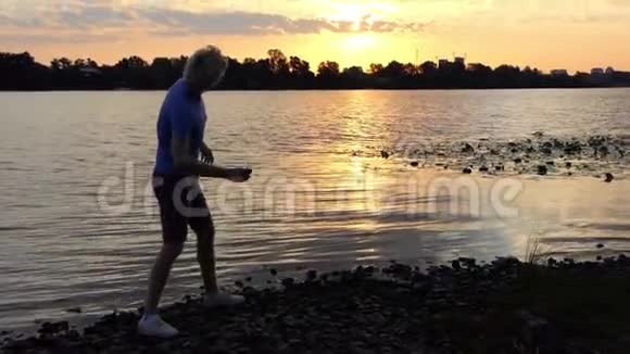 波光粼粼的夕阳和一个男孩扔在河里的石头视频的预览图