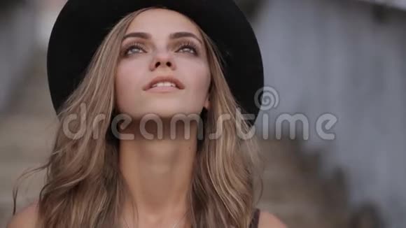 一个戴着黑帽子的年轻漂亮女孩在灰色背景下抬头看视频的预览图