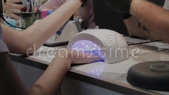 一个年轻的女孩在美甲沙龙的紫外线灯下干指甲油视频的预览图