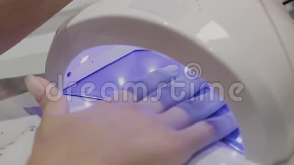 一个年轻的女孩在美甲沙龙的紫外线灯下干指甲油视频的预览图