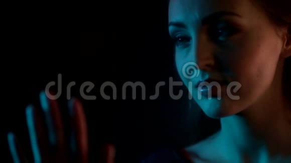 梦中迷人的白种人年轻女子望着玻璃窗用指尖在夜蓝色的霓虹灯中画出一颗心视频的预览图