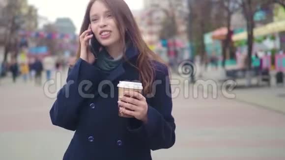 多莉拍摄的迷人混合种族女孩交谈智能手机和喝咖啡散步在城市街道年轻女子视频的预览图