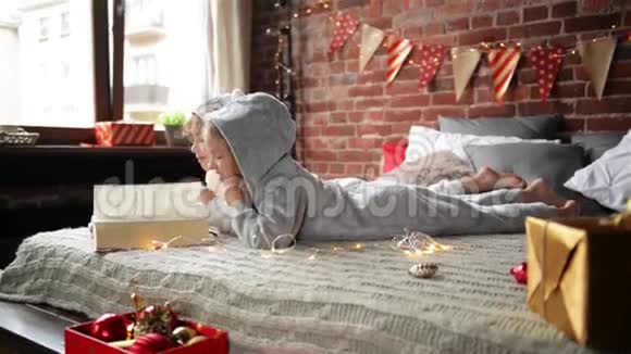 孩子们穿着温暖的圣诞睡衣坐在床上看书装饰圣诞节和圣诞节视频的预览图