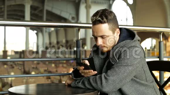 一个年轻人在一个大型购物中心的咖啡馆里用电话喝咖啡视频的预览图