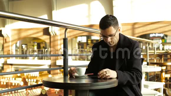 成年男性在咖啡馆里手里拿着手机喝咖啡视频的预览图