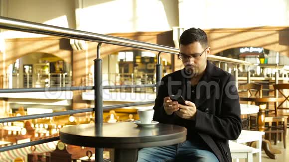 成年男性在咖啡馆里手里拿着手机喝咖啡视频的预览图