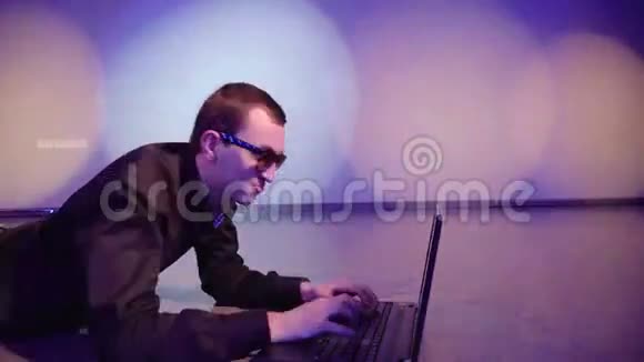 一个拿着笔记本电脑的年轻人躺在夜总会的地板上视频的预览图