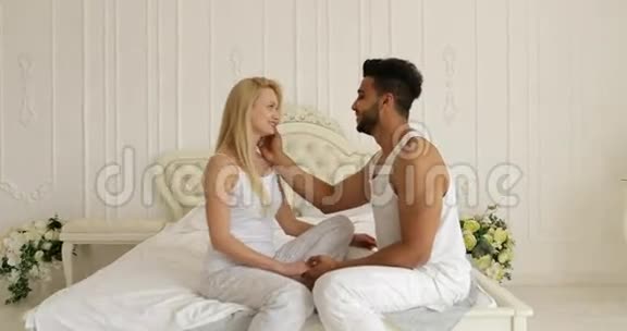情侣相爱相拥微笑坐床面对面混血男人抚摸女人脸拥抱早间卧室视频的预览图