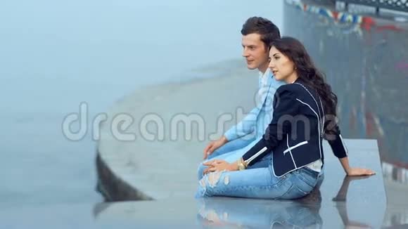 年轻的一对夫妇在河堤边坐着笑着说视频的预览图