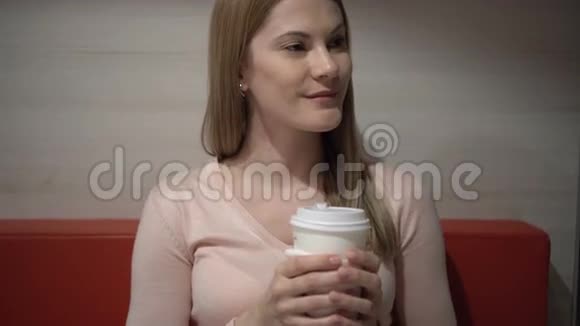 美丽迷人的年轻女人在咖啡馆里喝咖啡晚上好纸咖啡杯红色沙发视频的预览图